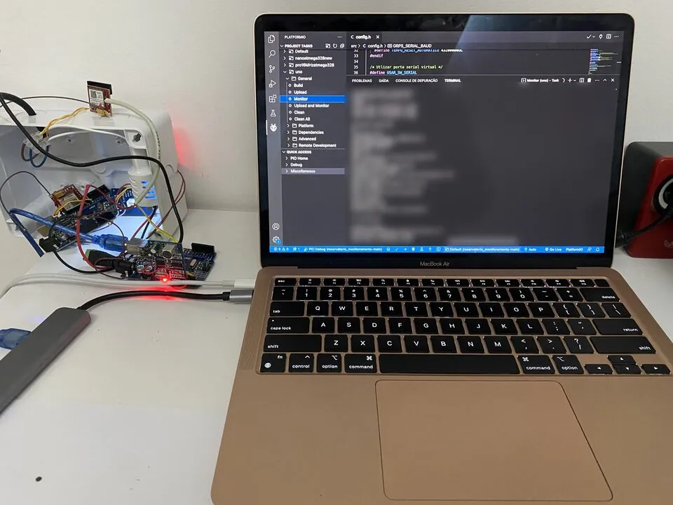 Notebook com código de firmware aberto, ligado a placas eletrônicas na bancada